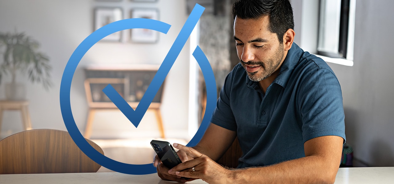 Man sitting at counter looking at phone with check mark logo on image