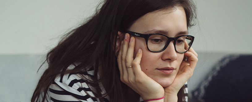 Young woman with glasses sitting with her head in her hands.
