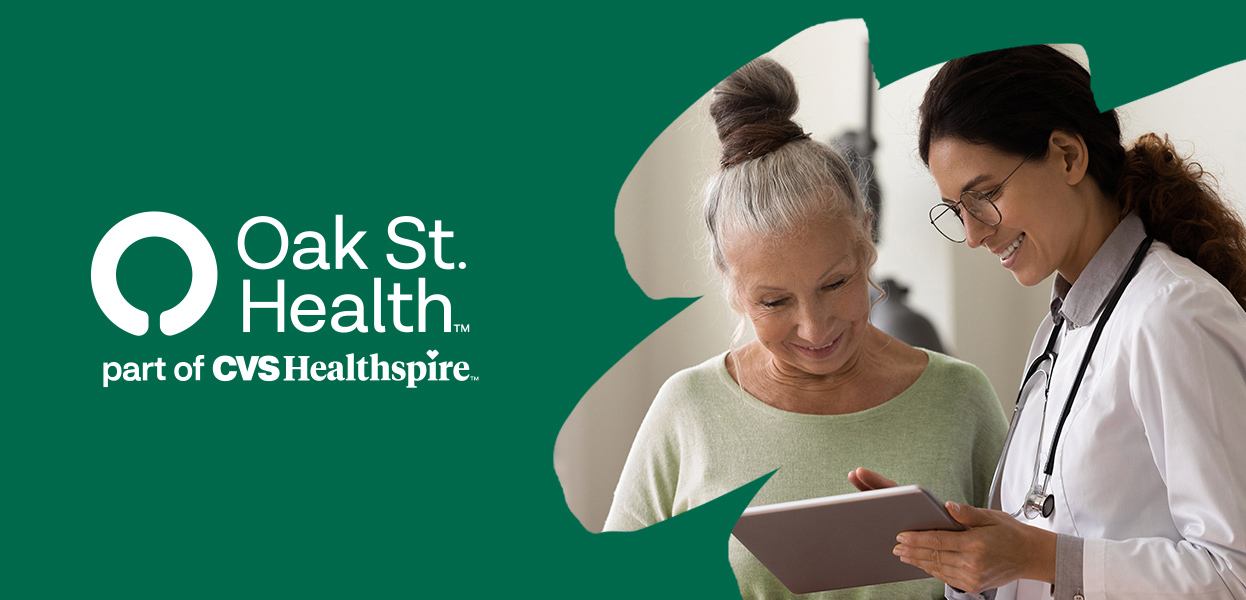 Smiling doctor reviewing information on computer screen with patient over 60 years of age, Oak St. Health logo, part of CVS Healthspire