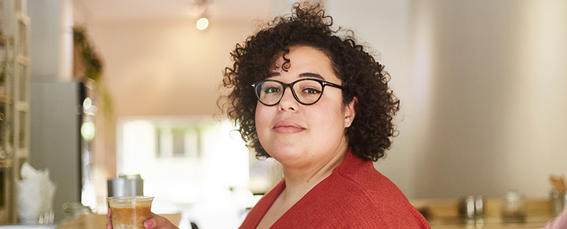Woman with curly hair standing in her kitchen with coffee