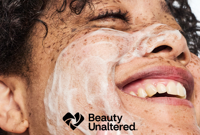 Beauty Unaltered logo. Close-up of a person looking upward with eyes closed and skin care lather on their face.